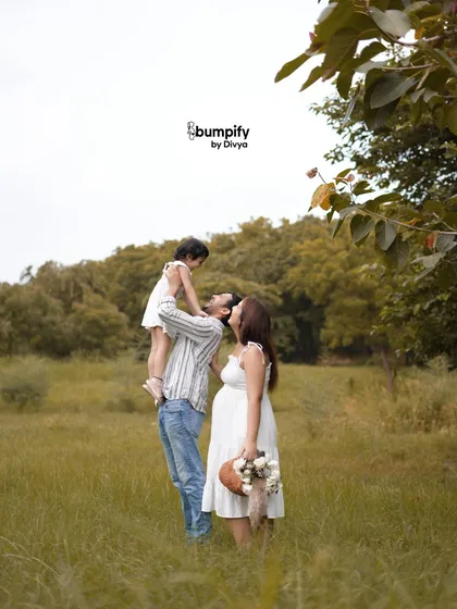 A playful and loving moment as the father lifts his daughter up for a kiss, while the mom-to-be watches with a smile. These candid moments make for the best memories.
