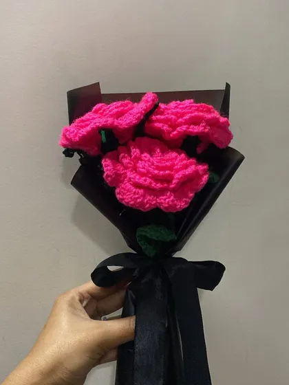 Holding the finished bouquet of three vibrant pink carnations. The black ribbon provides a simple and elegant finishing touch.