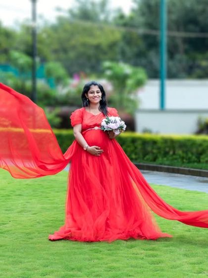 A beautiful shot of a red gown with a long, flying train in a green park.