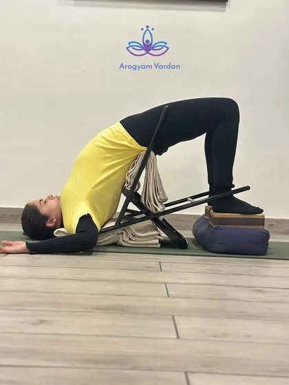 This is Chatushpadasana (Four-Footed Pose) using a chair and blocks for support. This modification helps build strength in the back and legs while ensuring the neck and shoulders remain relaxed. It is an excellent preparation for deeper backbends.