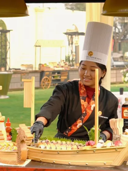 One of our talented chefs at the live sushi counter, smiling as she meticulously arranges a beautiful sushi boat display for an event.