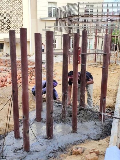 Workers pouring concrete foundations for a vertical play structure at the school site.