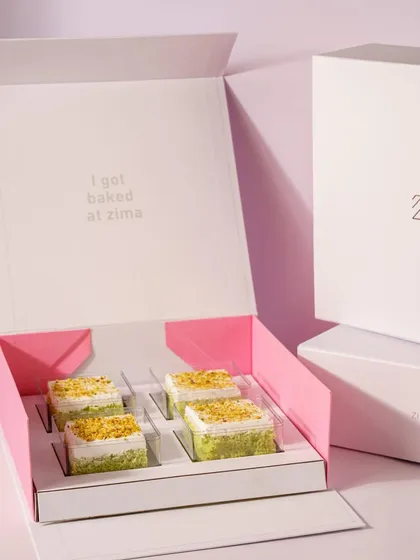 This shot showcases the unboxing experience of a dessert gift box. The clean lines and soft pink interior of the packaging, combined with the neatly arranged pistachio cakes, create a sense of luxury and anticipation.