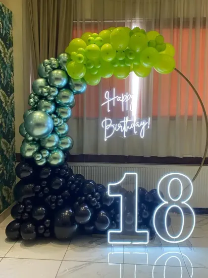 An 18th birthday with a unique black, green, and silver balloon arch and neon signs.