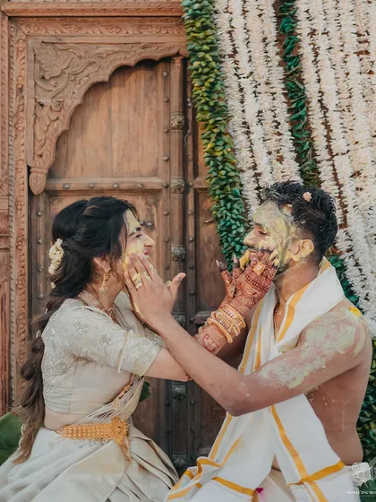 A playful moment from a South Indian Haldi, where the bride and groom lovingly apply turmeric paste to each other. The traditional attire and decor add to the authenticity of the celebration.