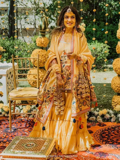 A full-length portrait of the bride looking radiant in her yellow outfit after the Choora and Kaleerey ceremonies.