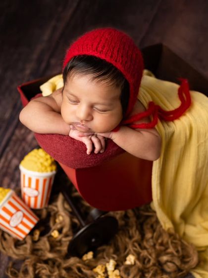 How cute is this little movie lover? This setup features a tiny wheelbarrow, popcorn props, and a cozy red hat for a fun and whimsical popcorn-themed shoot.