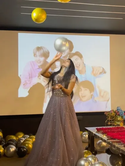 A fun, playful shot of the birthday girl with balloons, with a BTS photo on the big screen behind her. It shows how you can incorporate your favorite music and artists into your private party.