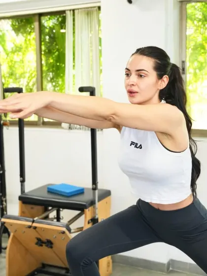 This client shows deep focus during a squat variation on the Pilates chair. This exercise builds lower body strength, balance, and control, fundamental components of fitness.