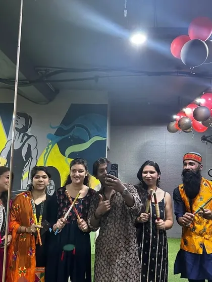 A group of members and trainers posing with their dandiya sticks under the festive decorations.