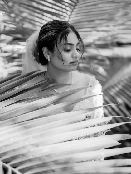 An artistic black and white portrait of the bride amidst palm leaves.