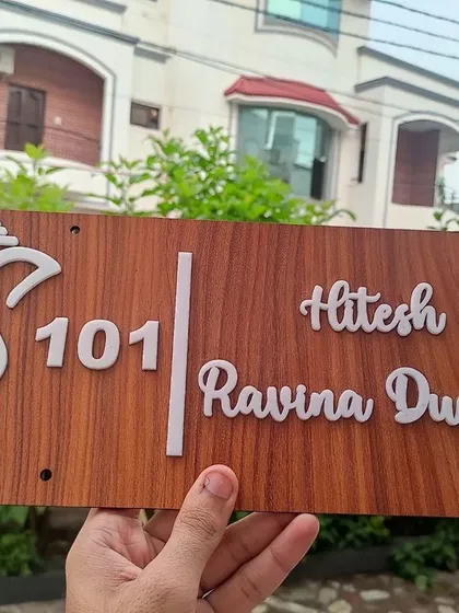 Welcome guests with a custom wooden door nameplate. This design features a traditional Ganesha motif alongside the family names and flat number, adding a personal and auspicious touch to your home's entrance.