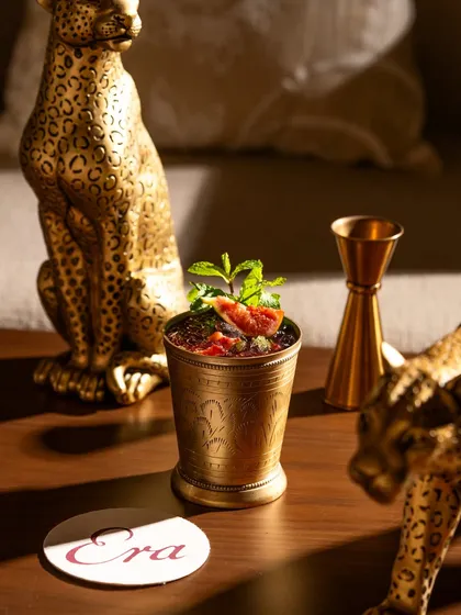 A brass julep cup with fresh mint and fig, styled with gold accents. This shot creates a sense of luxury and opulence.