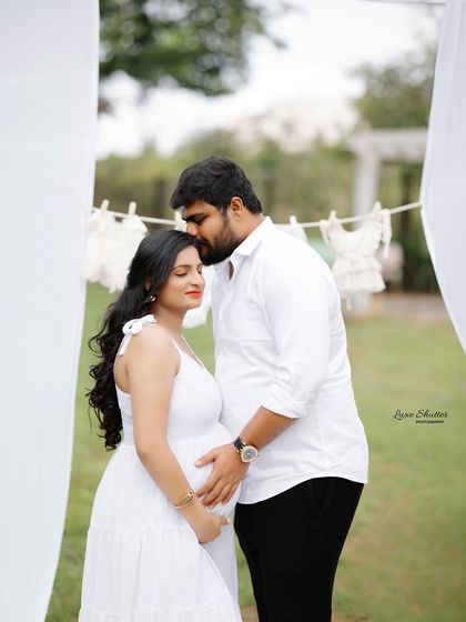 A beautiful, intimate moment during an outdoor session. The husband gently kisses his wife's forehead, surrounded by the soft, natural light and greenery.