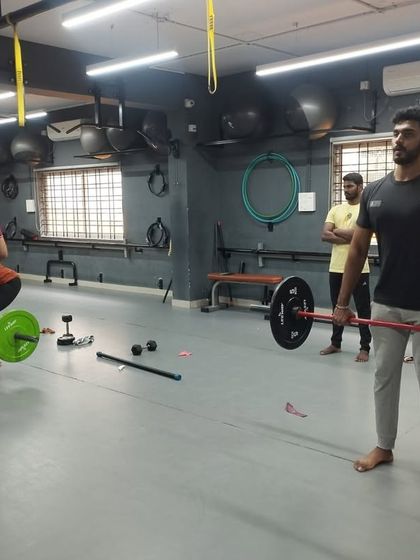 A student practices a barbell lift, focusing on maintaining proper posture and control throughout the movement.