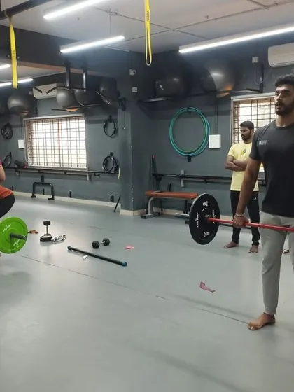 A student practices a barbell lift, focusing on maintaining proper posture and control throughout the movement.
