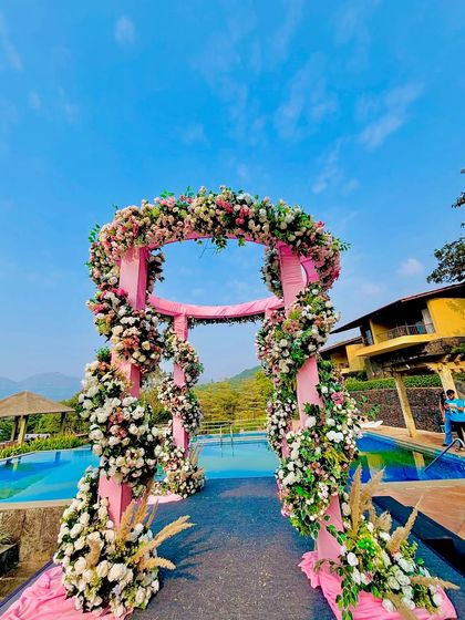A closer view of the poolside floral mandap, highlighting the lush flower arrangements and the beautiful contrast with the bright blue sky and water.