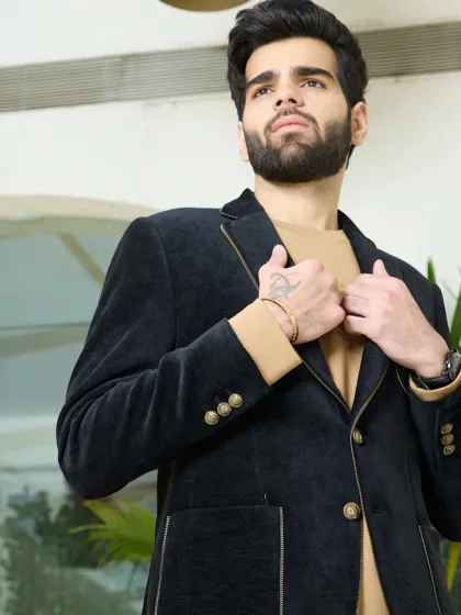 The black corduroy blazer, shown here being fastened, highlights the elegant gold buttons and the rich, velvety texture of the fabric.