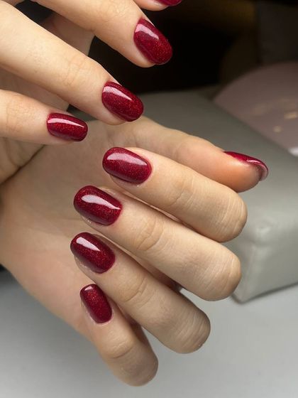 A beautiful shimmery red polish on short, rounded nails. The glitter is fine and evenly distributed, creating a sophisticated sparkle.
