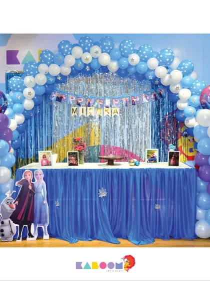 A classic Frozen party setup with a shimmering silver and blue balloon arch, character cutouts of Anna, Elsa, and Olaf, and a beautifully decorated main table fit for royalty.
