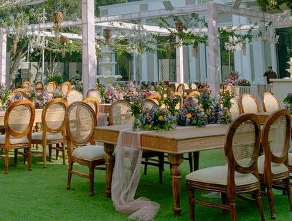 Elegant guest seating for a garden wedding, with long wooden tables, classic chairs, and sheer pink runners that complement the pastel floral theme.