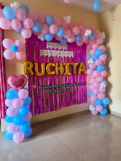 A pink and blue balloon arch decoration for a birthday, featuring a foil curtain and custom name balloons.