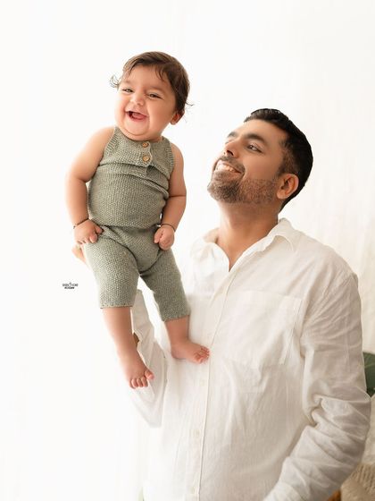 A father lifting his baby up, both of them sharing a huge smile.