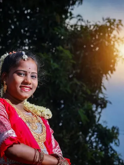 A bright and happy close-up portrait from an outdoor puberty ceremony shoot. Her beautiful smile is the centerpiece of this photo, framed by the blue sky and green trees.