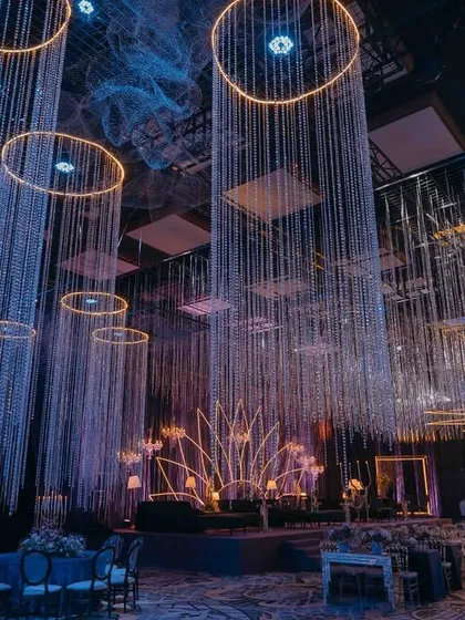 For this Sangeet night, I transformed the ballroom into a celestial wonderland. Thousands of crystal strings hang like a shimmering rain from illuminated rings, creating a dynamic and magical canopy above the celebration. This design blends light and texture to craft an atmosphere of pure, modern glamour.