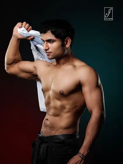 This shot uses a piece of clothing as a prop to create a dynamic line and add a sense of action. The lighting highlights the athlete's lean torso and defined abdominal muscles against a moody, colored background.
