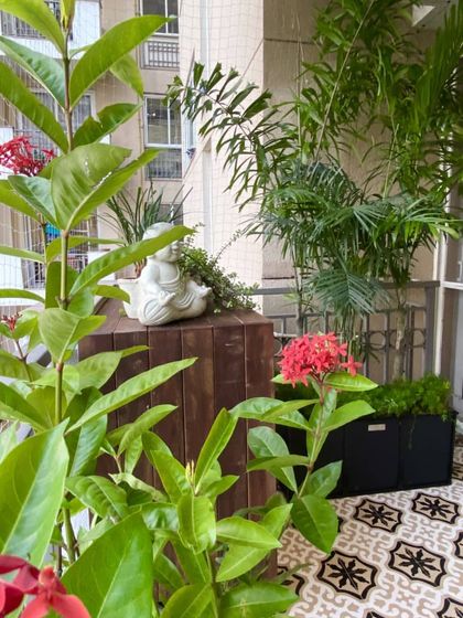 A close up of the plant styling, showing how we mix different textures and colors. The bright red Ixora flowers pop against the green leaves, and a small Buddha statue adds a touch of tranquility to the wooden cabinet.