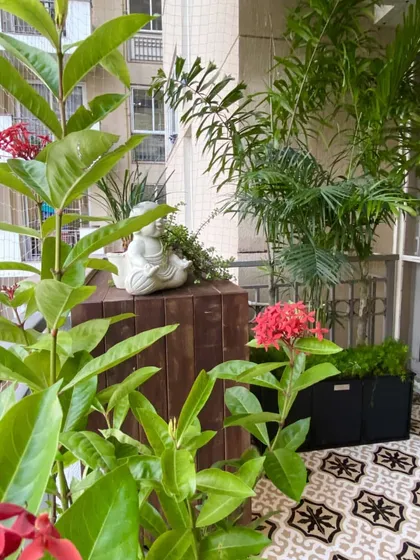 A close up of the plant styling, showing how we mix different textures and colors. The bright red Ixora flowers pop against the green leaves, and a small Buddha statue adds a touch of tranquility to the wooden cabinet.