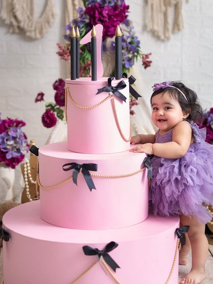 Standing tall by her birthday "cake". This shot captures the excitement and pride of a one-year-old in a beautifully coordinated purple and pink setting.
