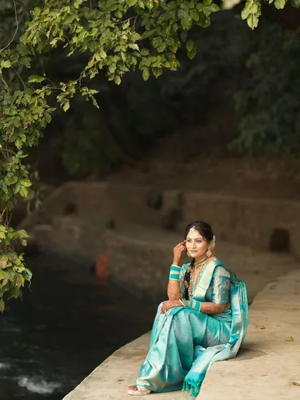 A serene shot of the bride sitting by the river, her beautiful blue silk saree spread around her. A moment of calm before the ceremony.