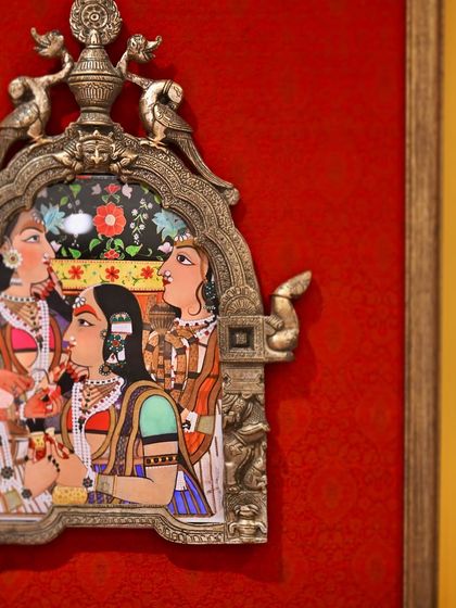 A close-up of the larger Prabhavali, featuring a scene from a painting of Maharaja Pratap Singh of Jaipur with the ladies of the royal harem. The artwork is framed in a vintage brass halo against a bold red silk.