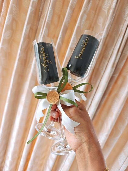 A pair of hand-engraved champagne flutes for a wedding, held up to show the delicate calligraphy of the bride and groom's names.