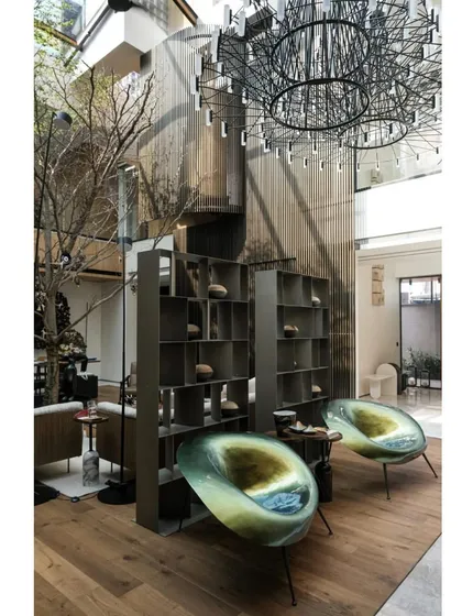 The interior of the retrofitted Mumbai home features a double-height space with a central tree, contemporary furniture, and a dramatic chandelier.