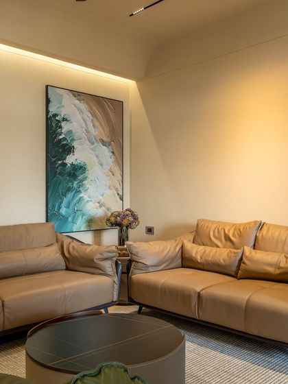 The main seating area with plush, tan leather sofas. A large abstract painting adds a splash of color, while cove lighting provides a warm, ambient glow to the room.