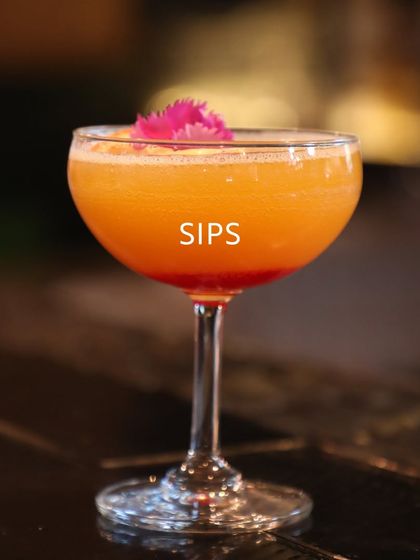 A close-up of a beautiful orange cocktail garnished with a pink flower. This image represents the artistic and flavourful sips that can accompany any conversation or meeting.