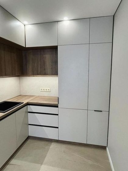 A view of the corner section, showing how the wood-grain upper cabinets create a warm contrast with the white lower units. The handle-less design maintains a clean and uncluttered look.