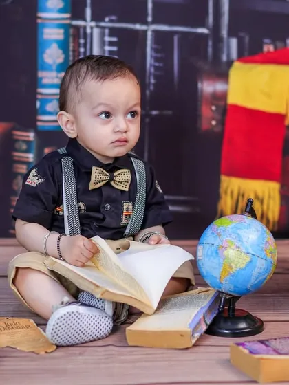A baby boy dressed as a little scholar, looking thoughtfully at a book in our vintage library setup.