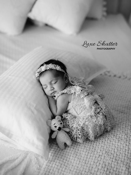 A classic black and white newborn photo. The baby is sleeping soundly on a soft pillow, showcasing the delicate features and peacefulness of a newborn.
