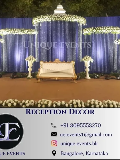 This outdoor reception stage showcases a modern and elegant design. We used a deep blue backdrop with cascading white floral and crystal strings, complemented by classic white urns and uplighting to create a sophisticated look.
