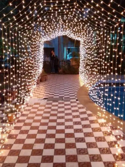 An ethereal entrance tunnel made entirely of warm fairy lights, creating a sparkling pathway next to a pool for a nighttime event.