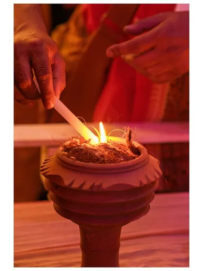 A hand lights the coconut husk and incense inside a dhunuchi pot, the beginning of the evening ritual dance.