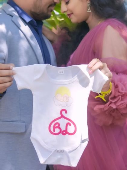 A close-up shot focusing on a baby onesie held by the expecting parents. This is a creative and personal way to announce your pregnancy during an outdoor shoot.