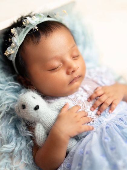A close-up of a baby girl in a lovely blue dress, cuddling a small teddy bear. The soft blue tones create a very serene and sweet image.