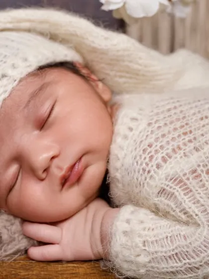 A close-up shot of a sleeping newborn in a soft, white knit outfit, showcasing their delicate features and peaceful expression.