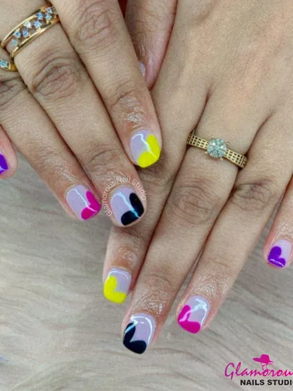 A vibrant and playful manicure with a mix of colors and abstract shapes, including yellow, pink, purple, and black on a sheer base.