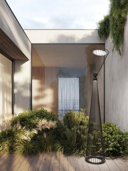 The Ikonika floor lamp is placed in an outdoor patio garden, demonstrating its suitability for exterior use. The lamp's form integrates seamlessly with the lush greenery.